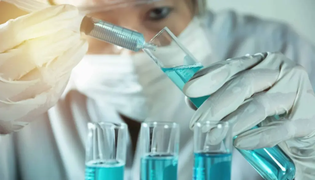 учёная производит манипуляции с голубоватой жидкостью в колбе с помощью шприца учёная производит манипуляции с голубоватой жидкостью в колбе с помощью шприца