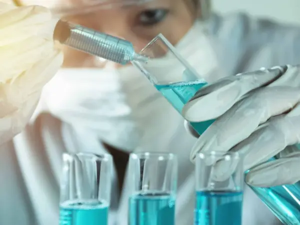 учёная производит манипуляции с голубоватой жидкостью в колбе с помощью шприца