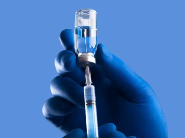 рука в перчатке набирает шприц из склянки с прозрачной жидкостью