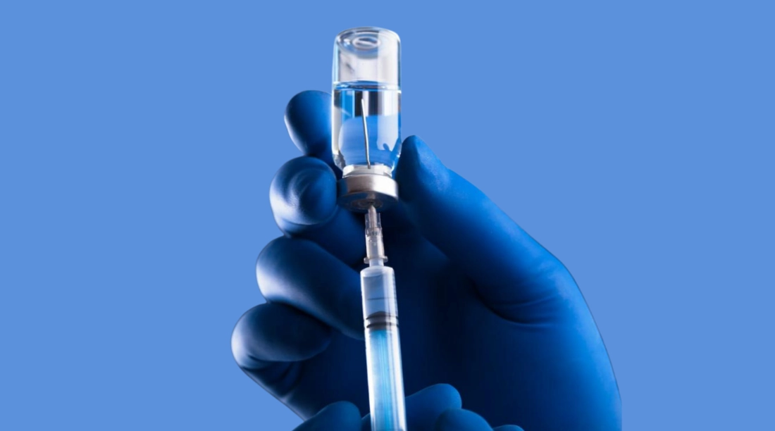 рука в перчатке набирает шприц из склянки с прозрачной жидкостью