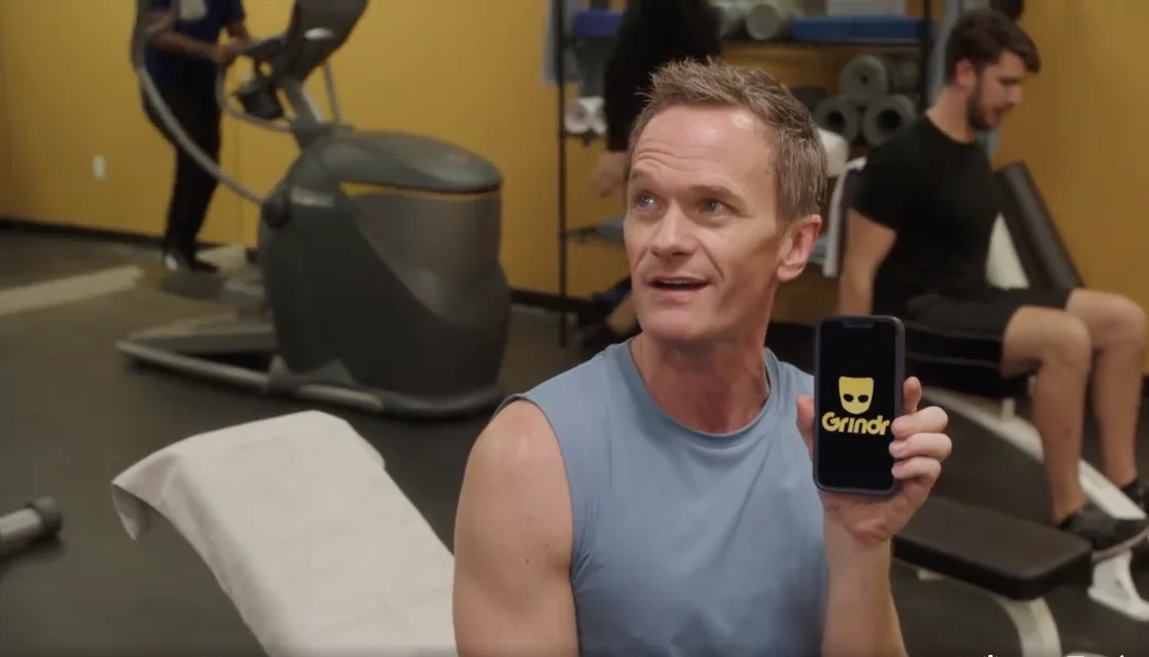 Мужчина в спортзале показывает телефон с заставкой приложения Grindr