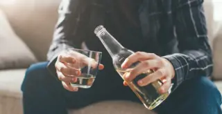 на изображении мужские руки, которые держат стакан и бутылку с алкогольным напитком