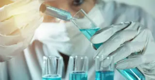 учёная производит манипуляции с голубоватой жидкостью в колбе с помощью шприца