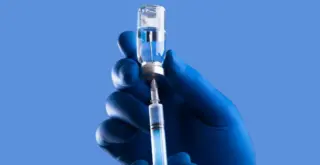 рука в перчатке набирает шприц из склянки с прозрачной жидкостью